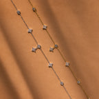 The Ivy Diamond Station Necklace in Silver sparkles with diamond accents, elegantly displayed on a warm brown background.