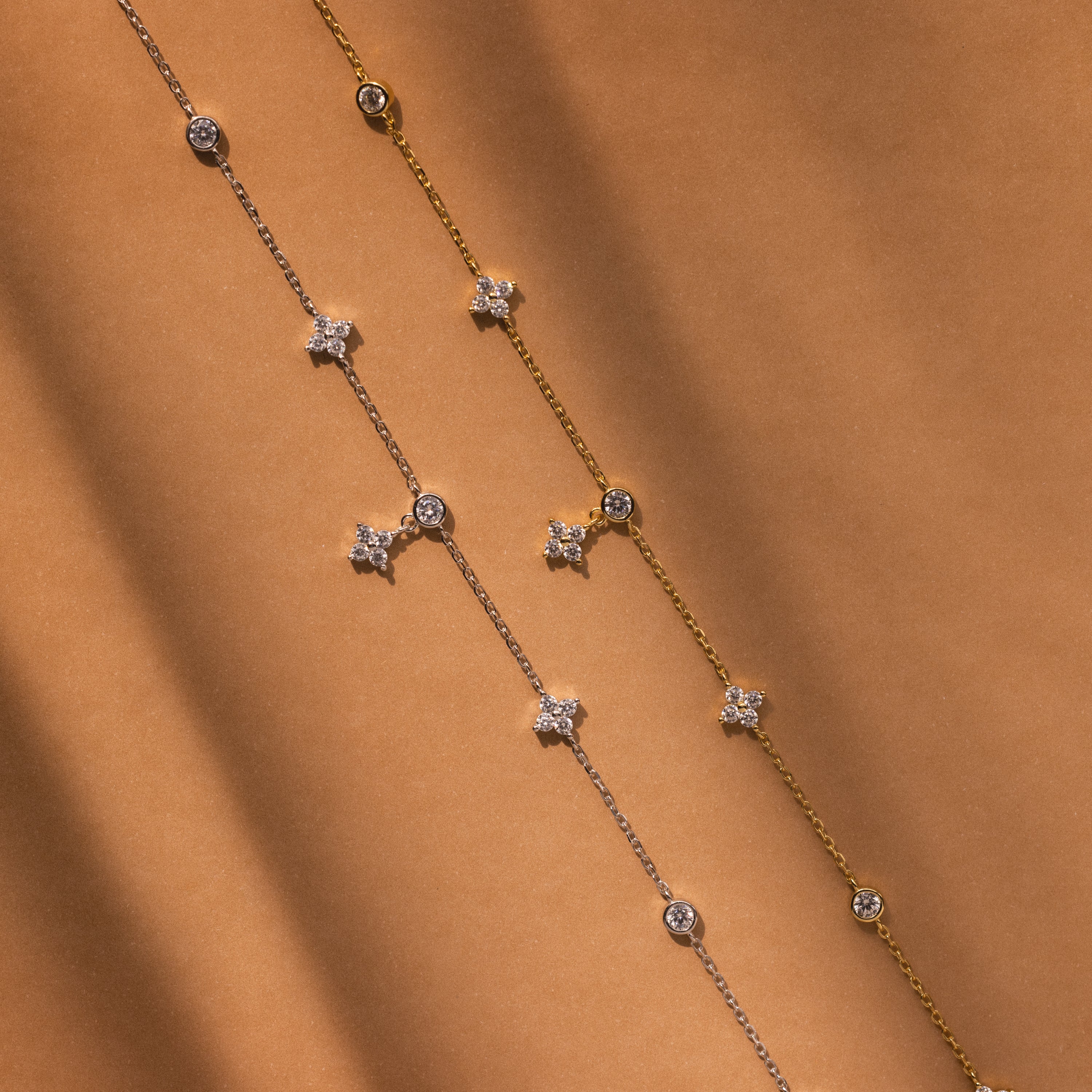 The Ivy Diamond Station Necklace in Silver sparkles with diamond accents, elegantly displayed on a warm brown background.