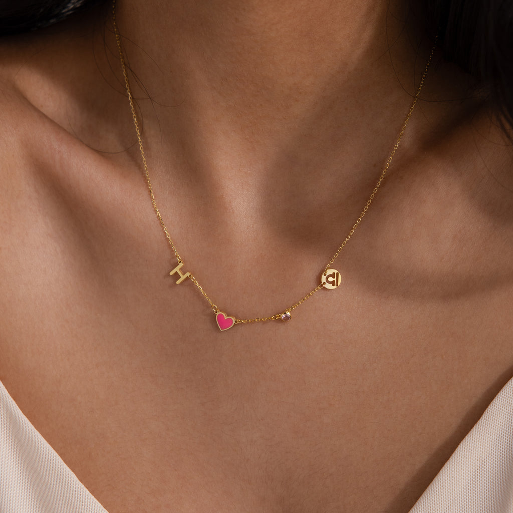 The Dainty Space Charm Necklace in 18K Gold features an “H,” a pink heart charm, and a round “C” pendant for a personalized look on your neck.