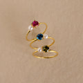 Three Birthstone & Pearl Rings with red, blue, and green gemstones plus pearls are arranged on beige. Each Birthstone & Pearl Ring is ideal for those who love elegant, personalized jewelry.