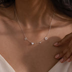 A woman wears the Dainty Space Charm Necklace in Sterling Silver, featuring personalized letter charms, a heart, and an ampersand on her bare neckline.