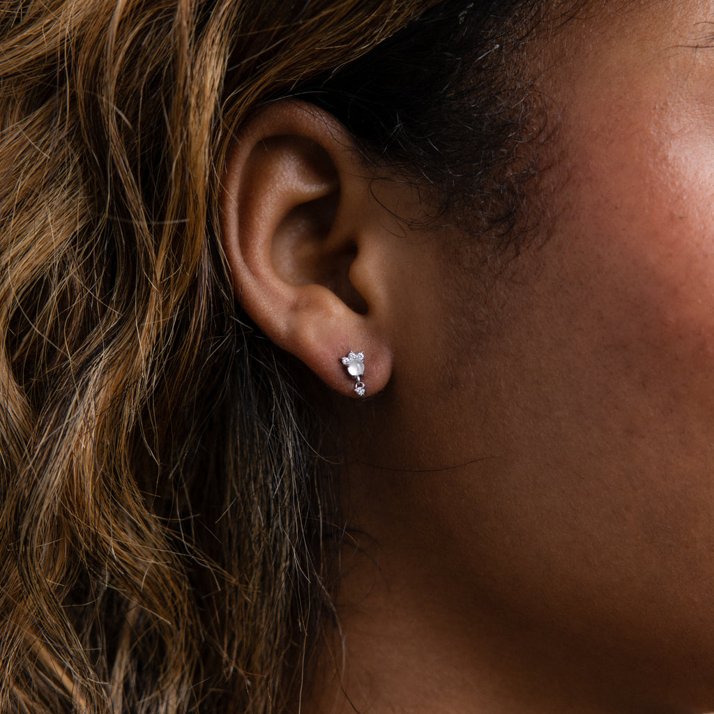 Close-up of a woman's ear wearing the Halo Moonstone Drop Studs in Sterling Silver, featuring three clear stones and exuding royal elegance in every detail.