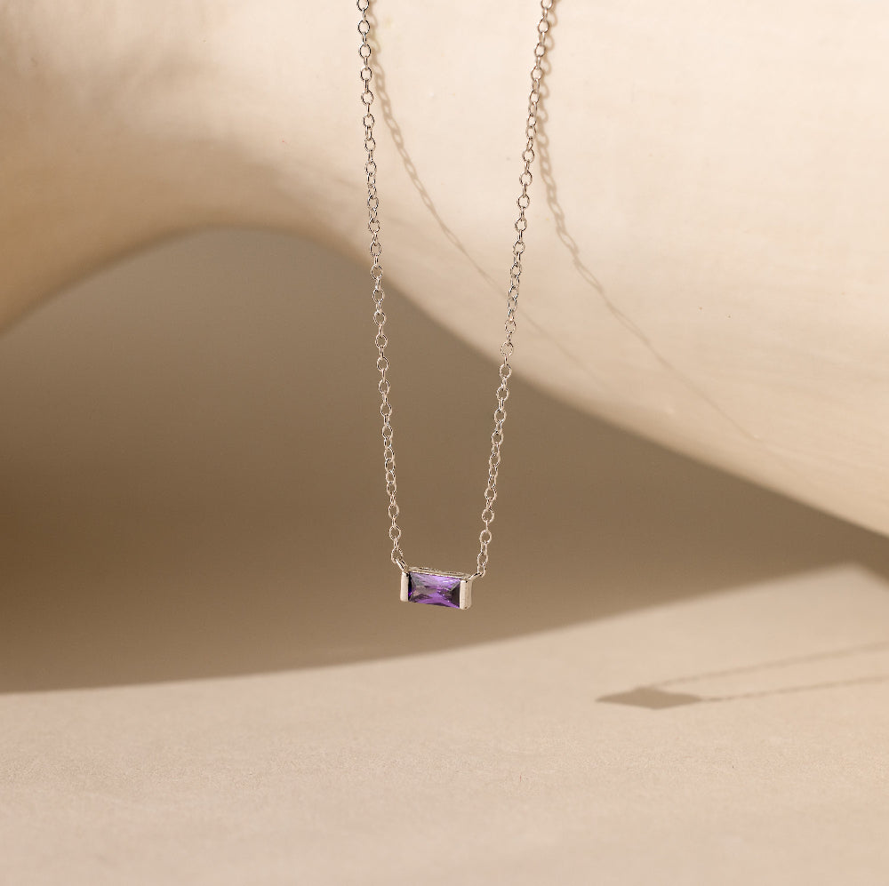 A silver Emery Birthstone Necklace featuring a rectangular amethyst gemstone, styled against a neutral-toned backdrop.