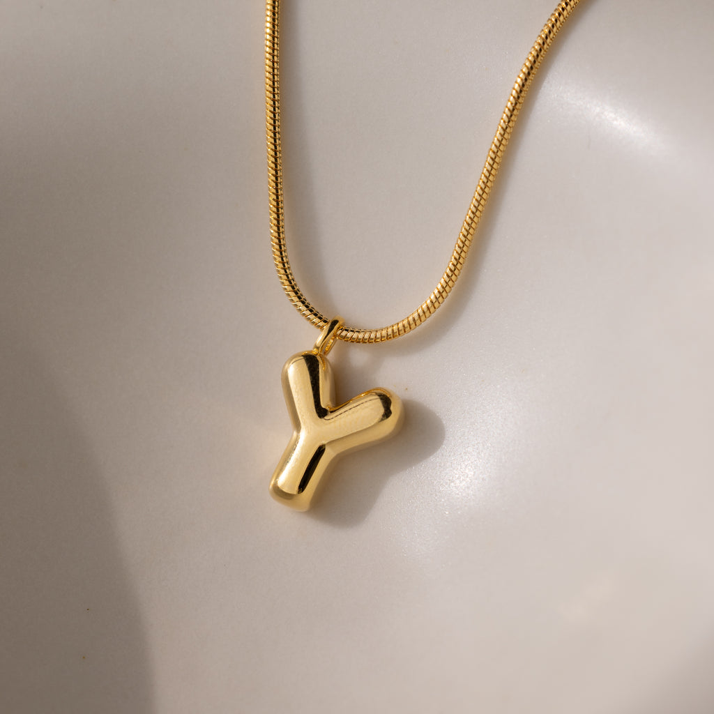 The Bubble Letter Necklace in 18K Gold features a shiny, smooth "Y"-shaped pendant—a chic, personalized jewelry piece—displayed on a soft, neutral background.