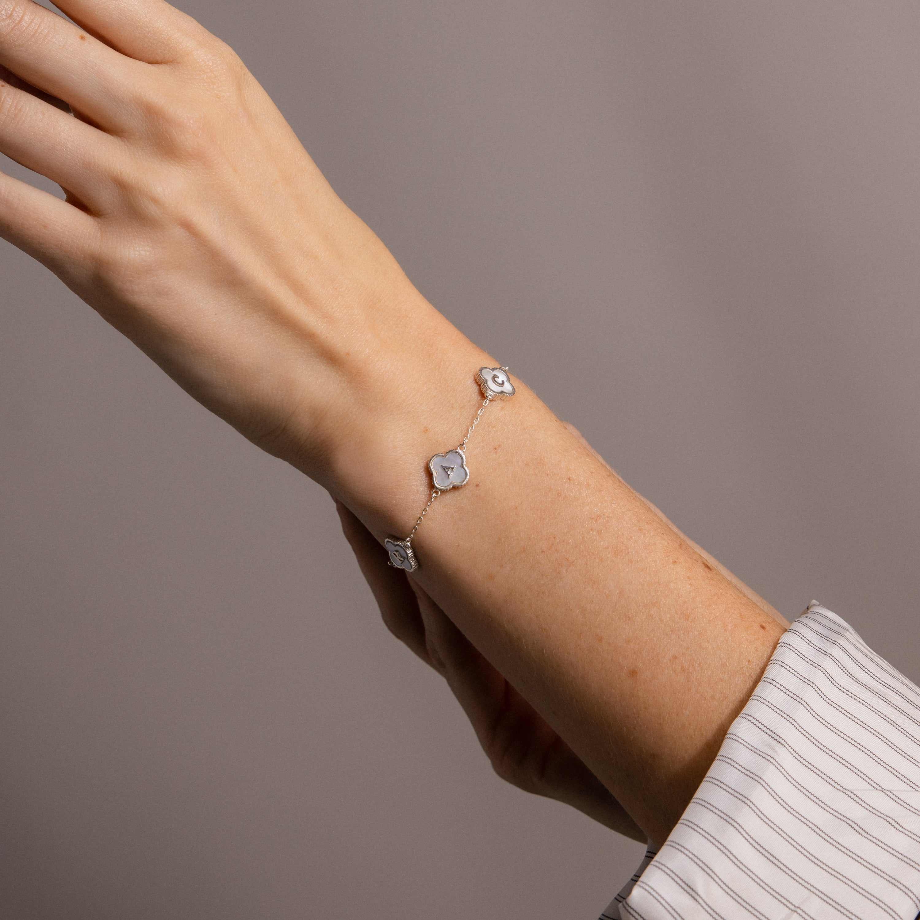 A hand wears the Pearl Clover Letter Bracelet in Sterling Silver, featuring three four-leaf clover charms, against a neutral background.