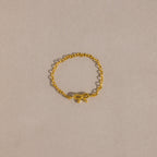 A delicate gold chain ring with a small, polished bow charm placed neatly on a soft beige background.