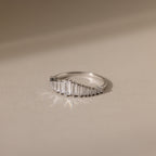 The Art Deco Diamond Ring in Sterling Silver features rectangular diamonds set in a curved line, casting a soft shadow on a beige surface—a striking statement piece.