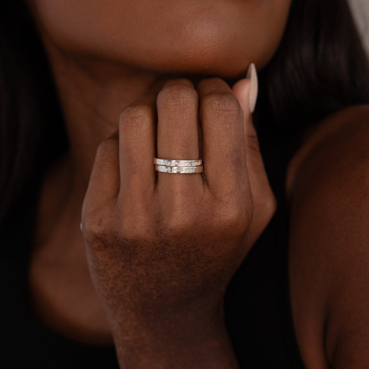 A close-up of a hand wearing two silver rings—one is the Ann Thin Message Ring in Sterling Silver—on the middle finger, set against a blurred background.