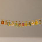 The Peridot Birth Flower Charm Necklace features a gold chain with twelve rectangular pendants, each adorned with vibrant floral and nature-inspired designs on unique backgrounds.