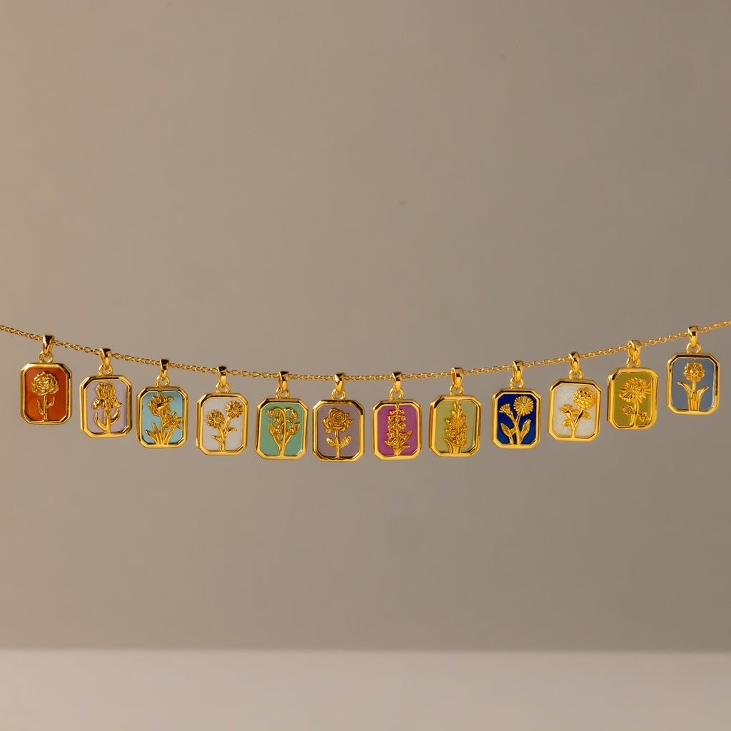 The Blue Zircon Birth Flower Charm Necklace features a gold chain adorned with twelve colorful rectangular pendants, each showcasing a unique floral design for a vibrant and elegant look.