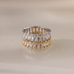 The Colette Eternity Ring features gold and silver bands with dual rows of baguette diamonds, exuding opulence against a neutral backdrop.