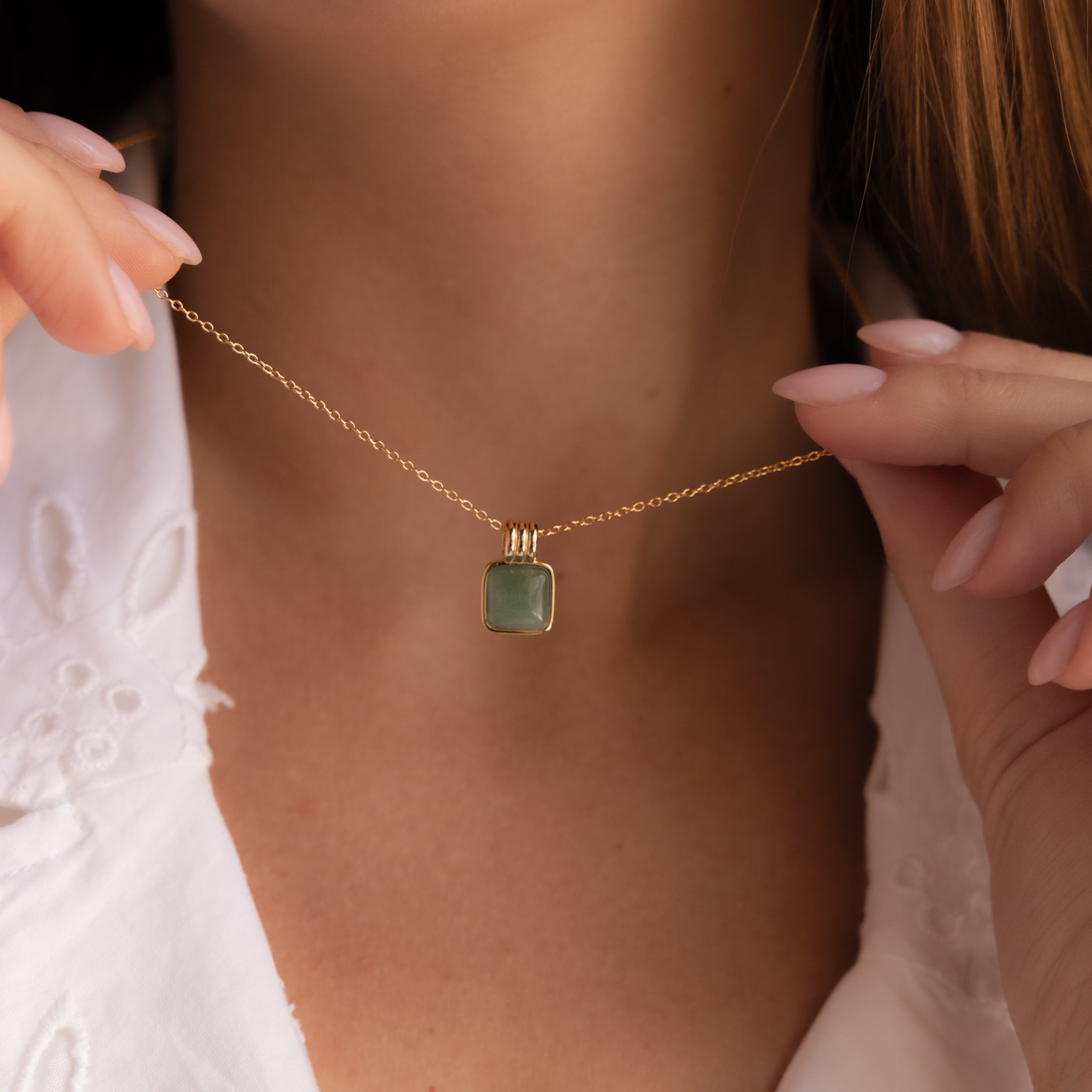 A woman wearing a white blouse holds the Jade Pendant Necklace featuring a square green jade stone that symbolizes new beginnings.