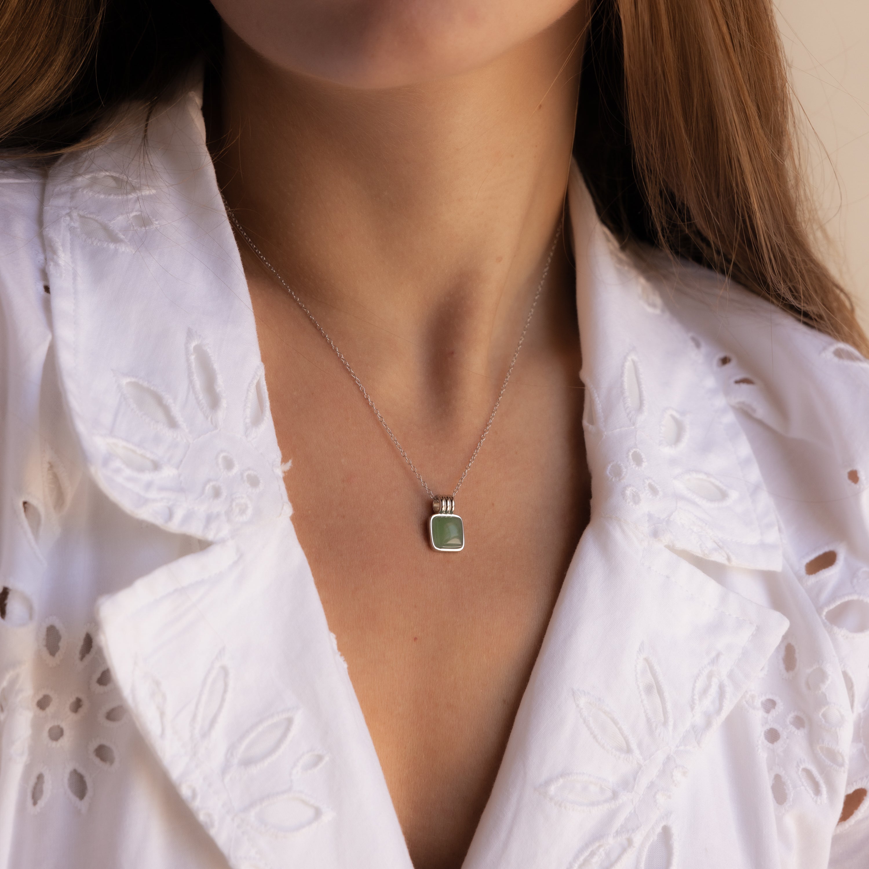 A woman wears a white eyelet blouse and the Jade Pendant Necklace, featuring a green jade stone that symbolizes new beginnings.