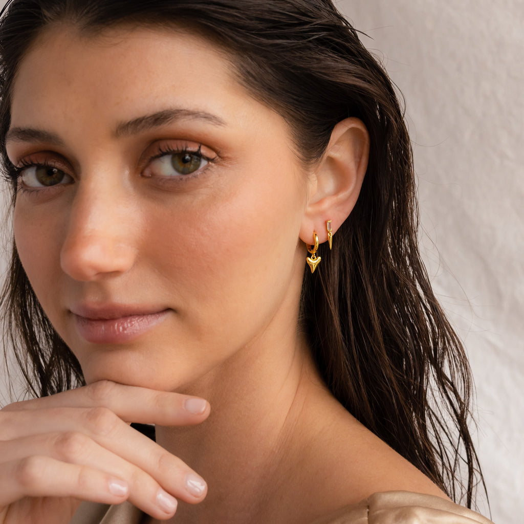 A woman with wet hair wears Shark Tooth Huggies, gazing at the camera with her hand by her chin—a laid-back look ideal for your next beach getaway.