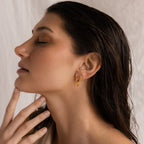 Woman with wet hair and eyes closed touches her chin, wearing Shark Tooth Huggies on a neutral background.