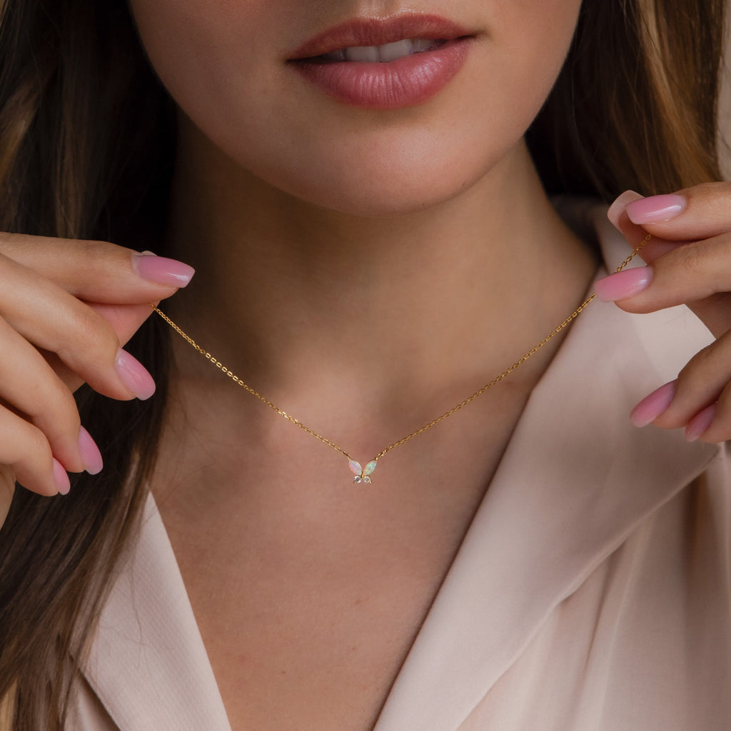 Woman wearing a delicate gold butterfly necklace with iridescent opal wings and small clear stone accents.
