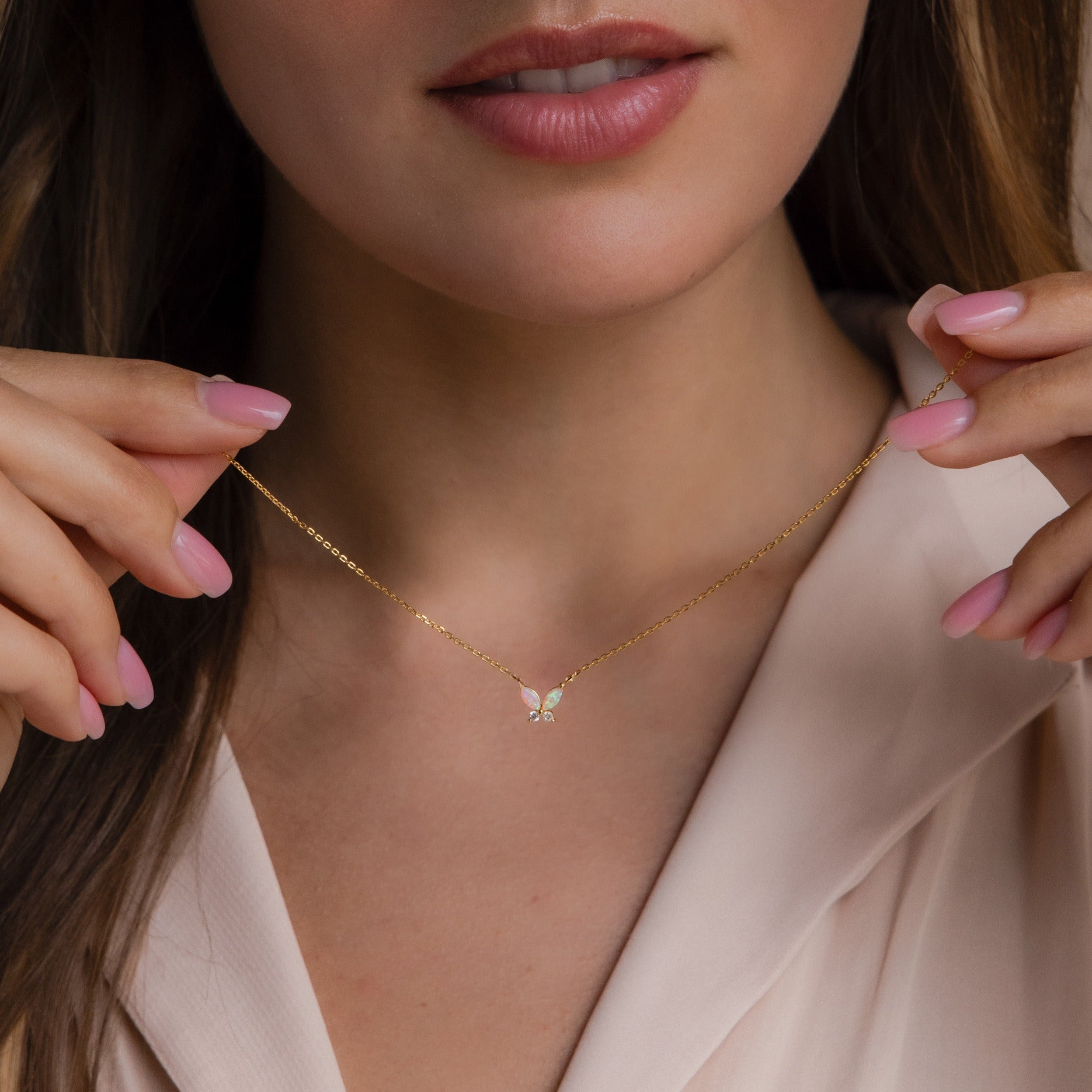 Woman wearing a delicate gold butterfly necklace with iridescent opal wings and small clear stone accents.
