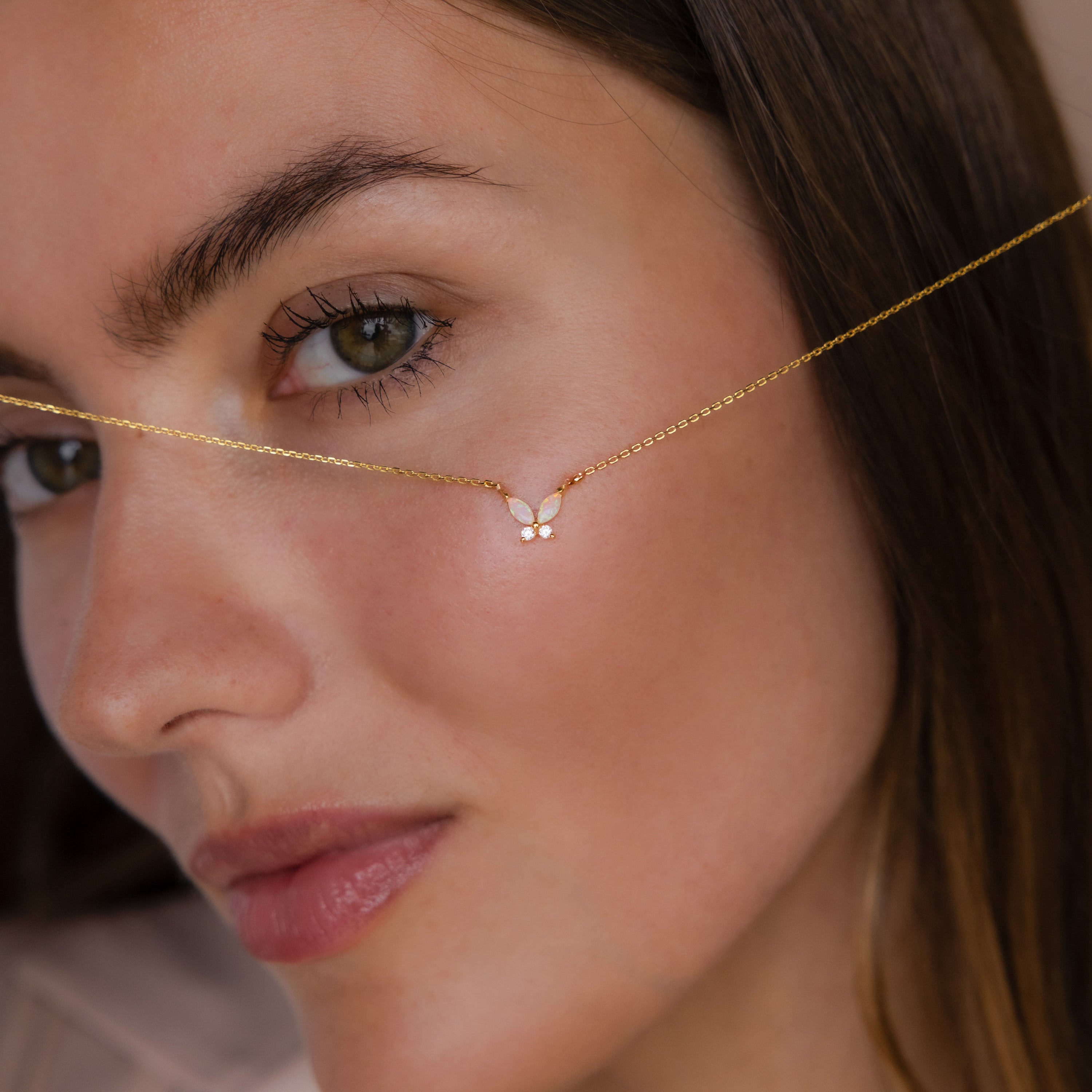 A woman holds the Pink Opal Butterfly Necklace in 18K Gold with a delicate butterfly pendant close to her face.