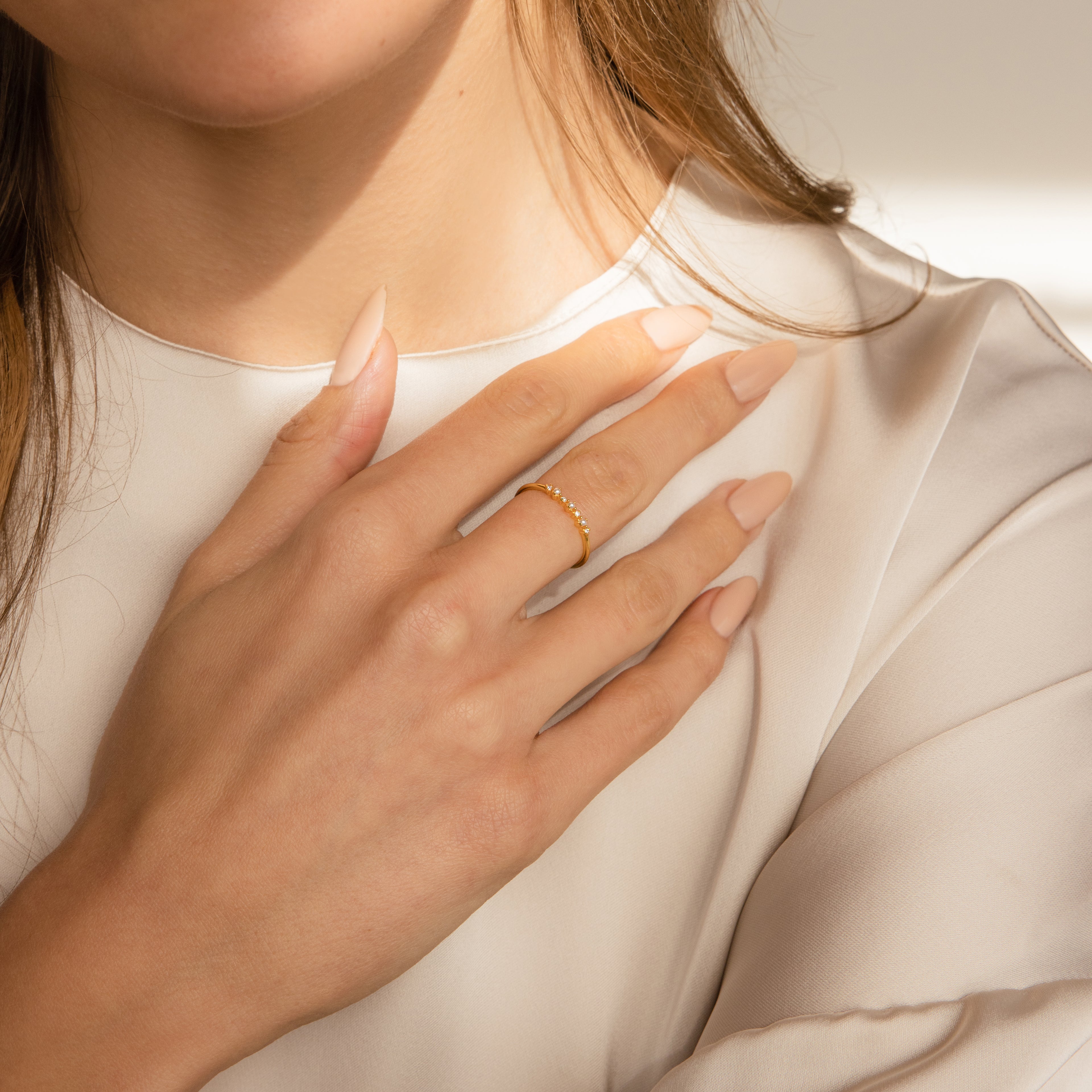 A woman with manicured nails gently touches her collarbone, wearing the Delicate Pearl Diamond Ring and a white blouse.