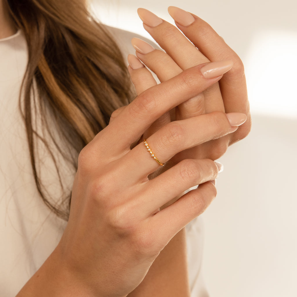 A woman with manicured nails wears the Delicate Pearl Diamond Ring in Silver on her finger, gently touching her hand.