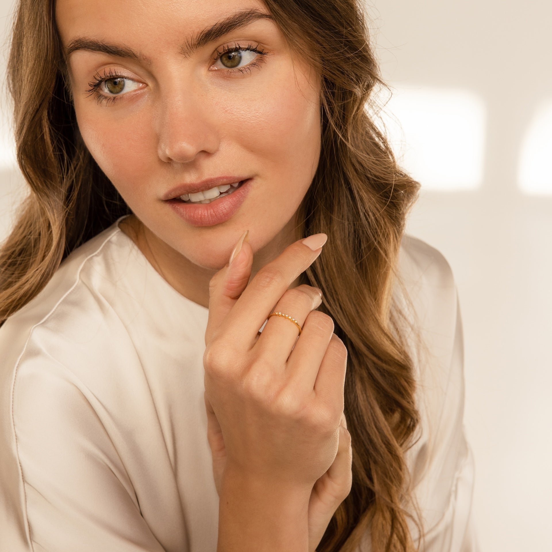 Woman with long brown hair in a cream blouse holds her hand near her face, showcasing the Delicate Pearl Diamond Ring.