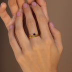 A hand with light pink nails wears the Black Abyss Ring Set—three stacked gold rings with dainty bands and a small black gemstone.