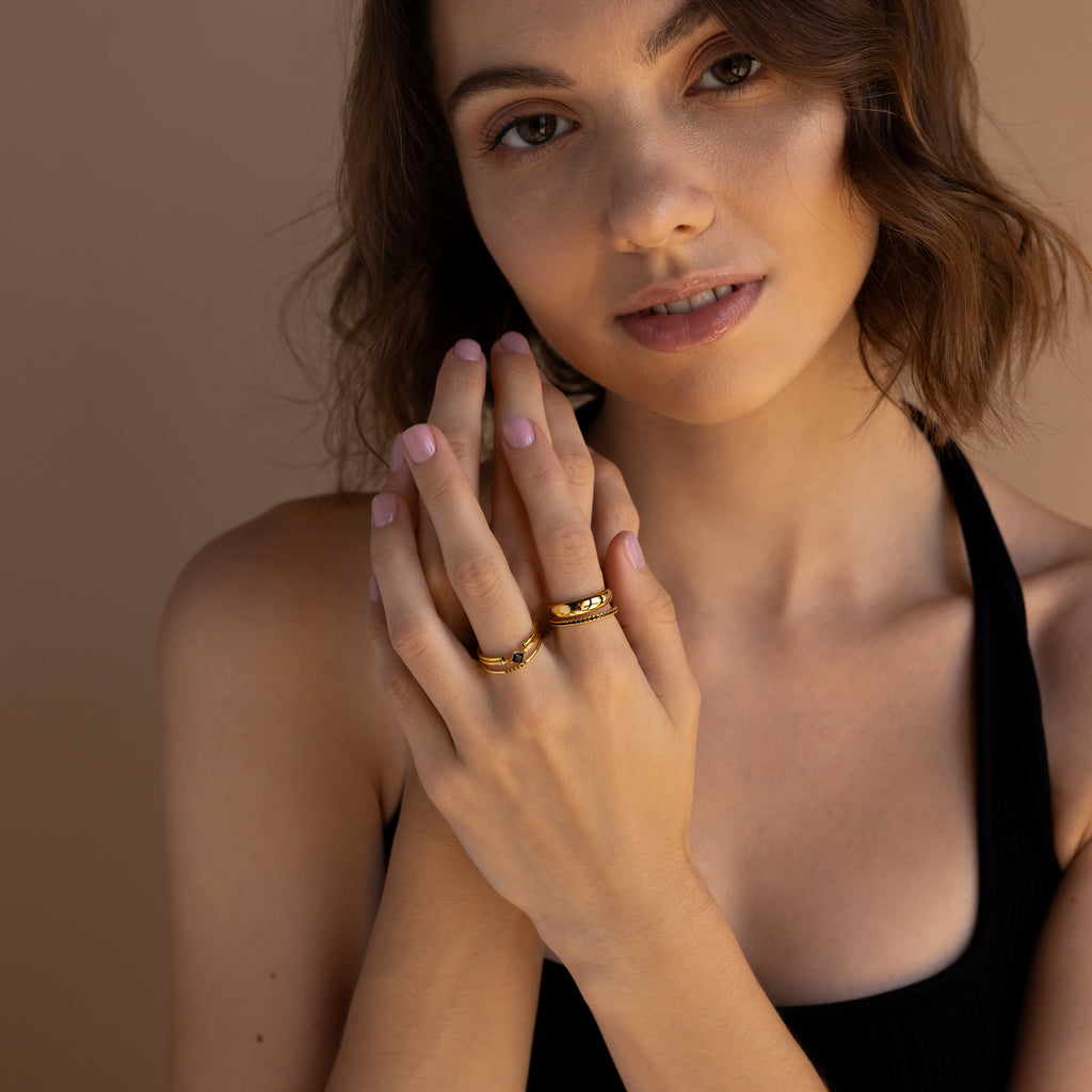 Woman with wavy brown hair wears delicate ring bands and the Black Abyss Ring Set, featuring black gemstones, near her face against a neutral background.