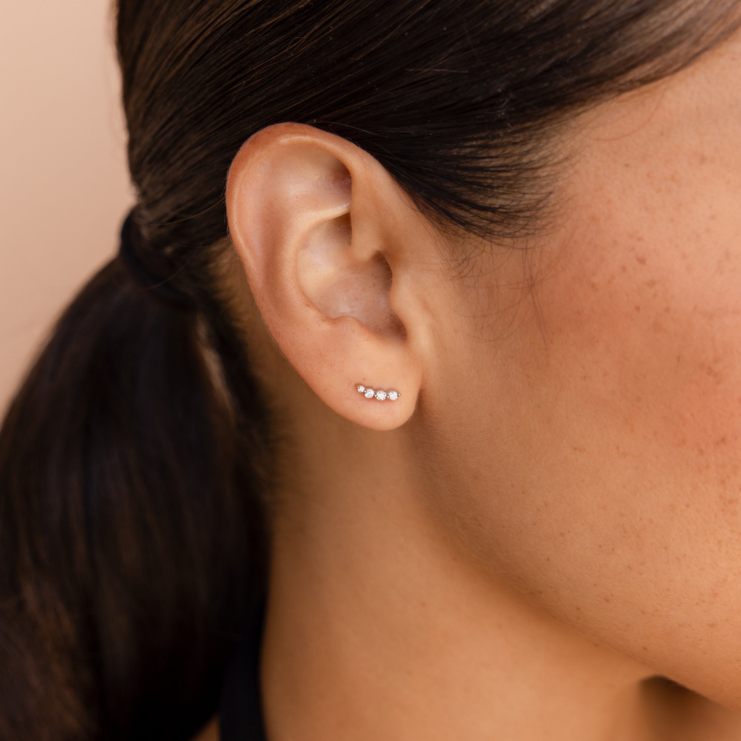 Close-up of an ear wearing a our diamond climber earring with three diamonds on a neutral background