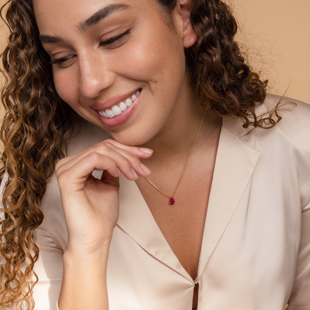 Smiling woman with curly hair wears a beige blazer and the Ophelia Blue Zircon Necklace, adding a minimalist touch to her look.