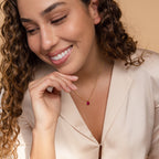 Smiling woman with curly hair wears a beige blazer and the Ophelia Blue Zircon Necklace, adding a minimalist touch to her look.