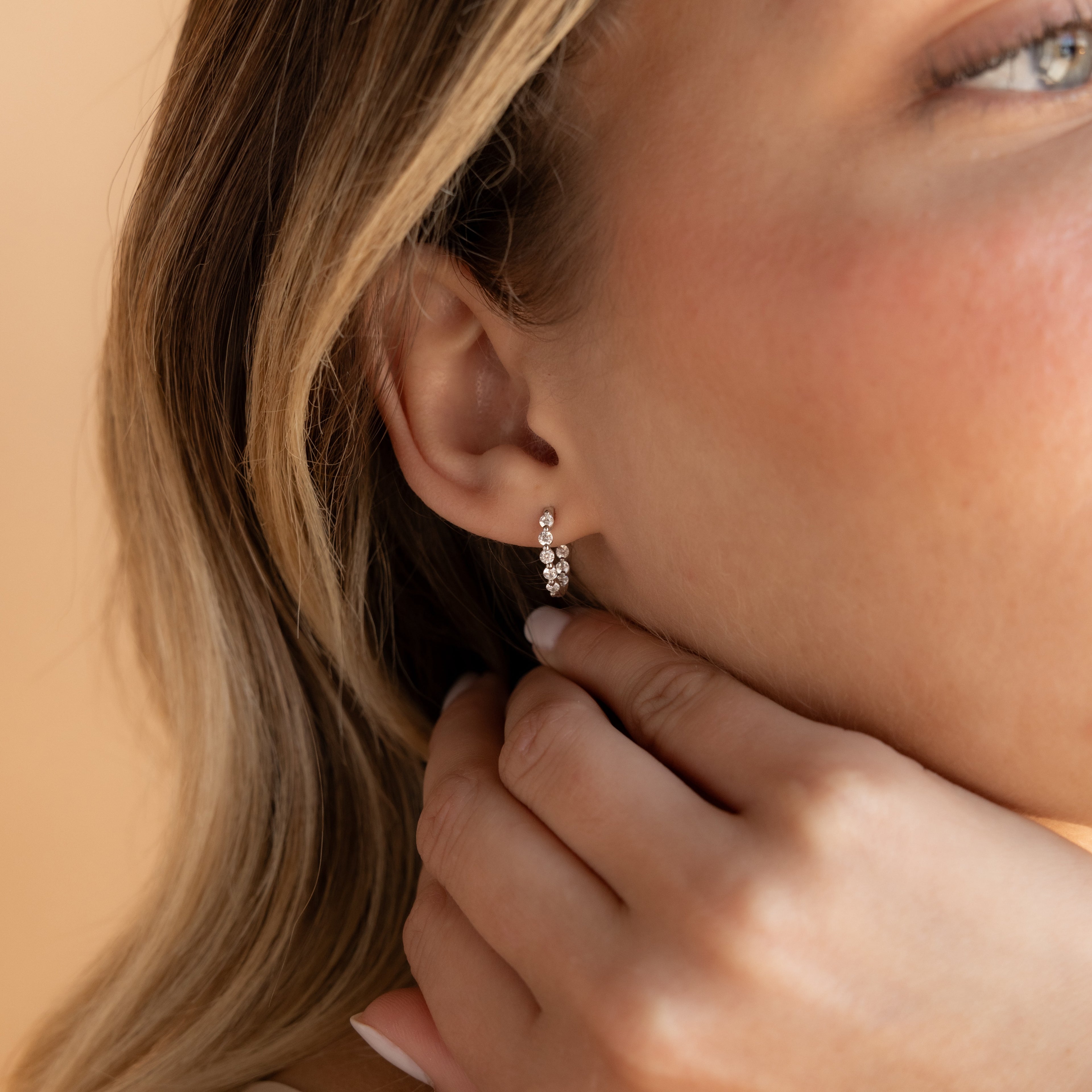 Close-up of a woman touching her ear, highlighting the Inside Out Diamond Huggies in Sterling Silver—small, elegant earrings adorned with sparkling diamonds.