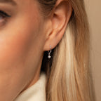 Close-up of a woman's ear wearing the Molly Pearl Huggies, small silver hoops featuring a delicate dangling pearl.