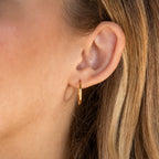 Close-up of a person’s ear wearing Medium Bold Hoops—small, thin gold hoop earrings ideal for lightweight, everyday jewelry. Light brown hair frames the earring.