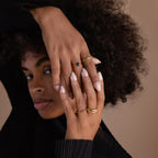 A woman with curly hair displays her hands wearing the Black Emerald Ring and gold bands against a neutral background.