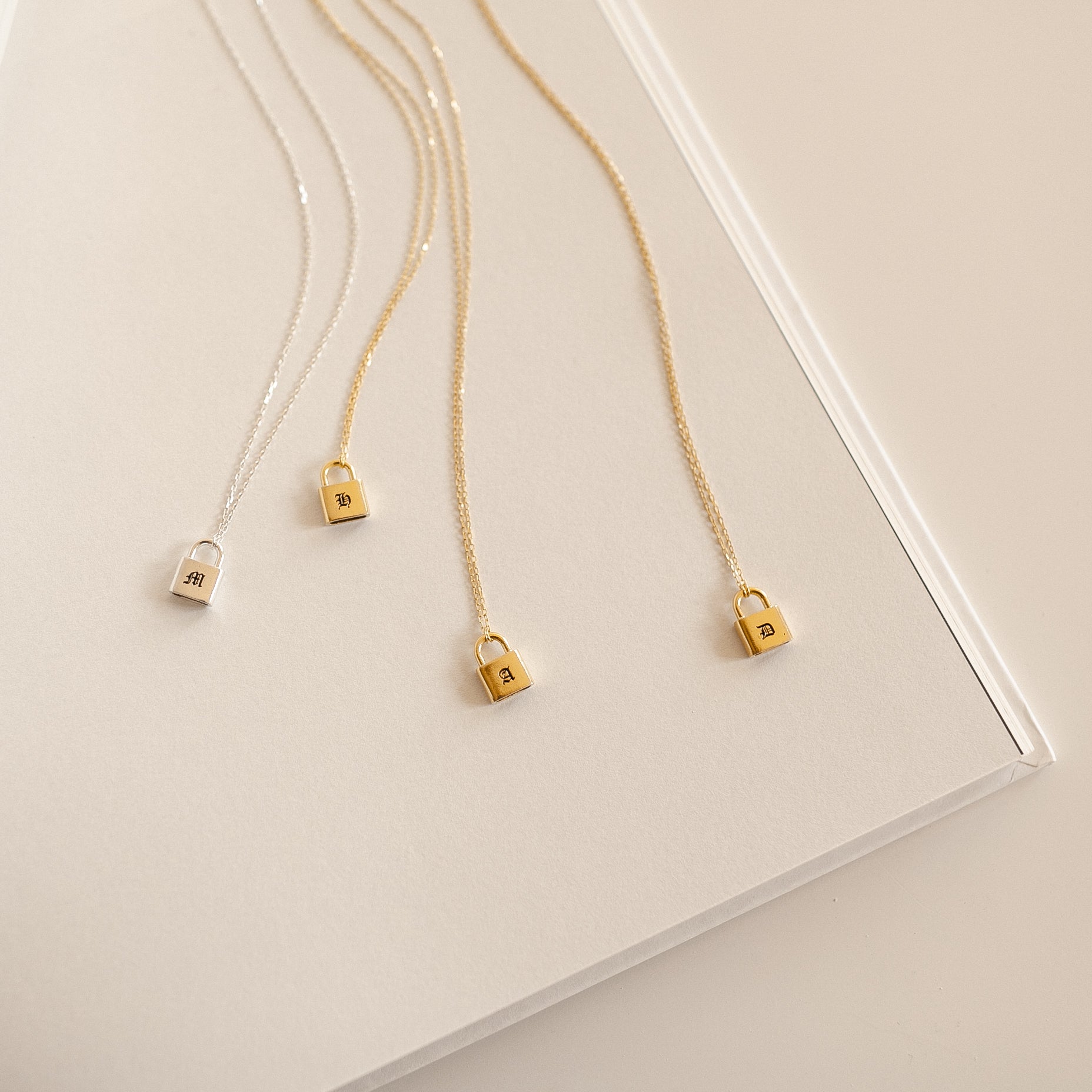 Gold and silver necklaces with lock pendants on a light beige surface
