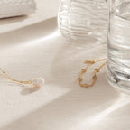 The Venus Diamond Station Bracelet rests on cream fabric beside a glass of water and a ribbed vase—an elegant choice for a wedding look or as an anniversary gift.