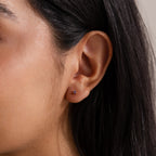 Close-up of a woman's ear with multiple piercings, featuring the Dainty Garnet Flatback Studs and dark straight hair.
