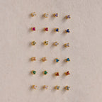 Twenty pairs of Dainty Amethyst Flatback Studs, ideal for multiple piercings, are displayed in a neat grid on a beige surface.