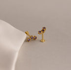 Alexandrite Cluster Flatback Studs featuring gold clusters and purple gemstones rest on a beige surface beside white fabric—ideal as personalized jewelry or birthstone earrings.