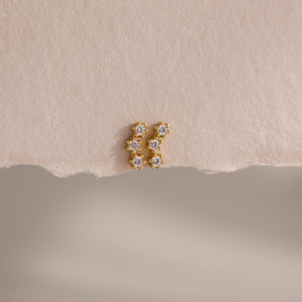 Diamond Cluster Flatback Studs with sparkling white gemstones are displayed on a textured beige surface.