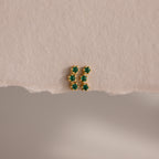 Emerald Cluster Flatback Studs: small gold earrings featuring six green stones in two vertical rows, shown on a textured beige surface.