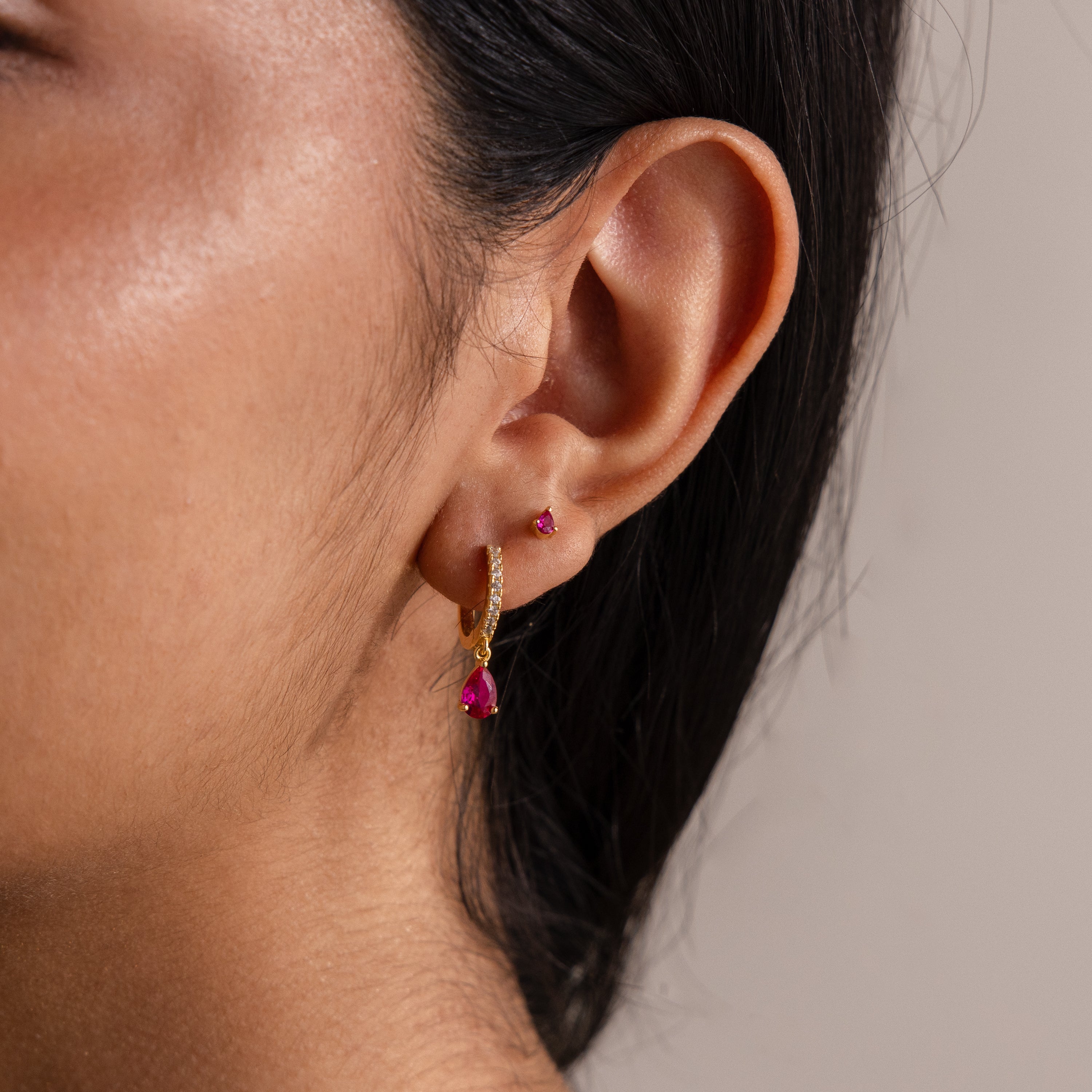 Close-up of a woman's ear wearing Teardrop Birthstone Flatback Studs featuring pink gemstones and a gold hoop—ideal for those who appreciate elegant Birthstone Jewelry.