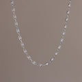 Close-up of a delicate silver chain necklace with oval pearl links, suspended against a neutral backdrop.