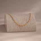 Pearl chain necklace draped over a textured display stand, softly lit in a warm, minimal setting.