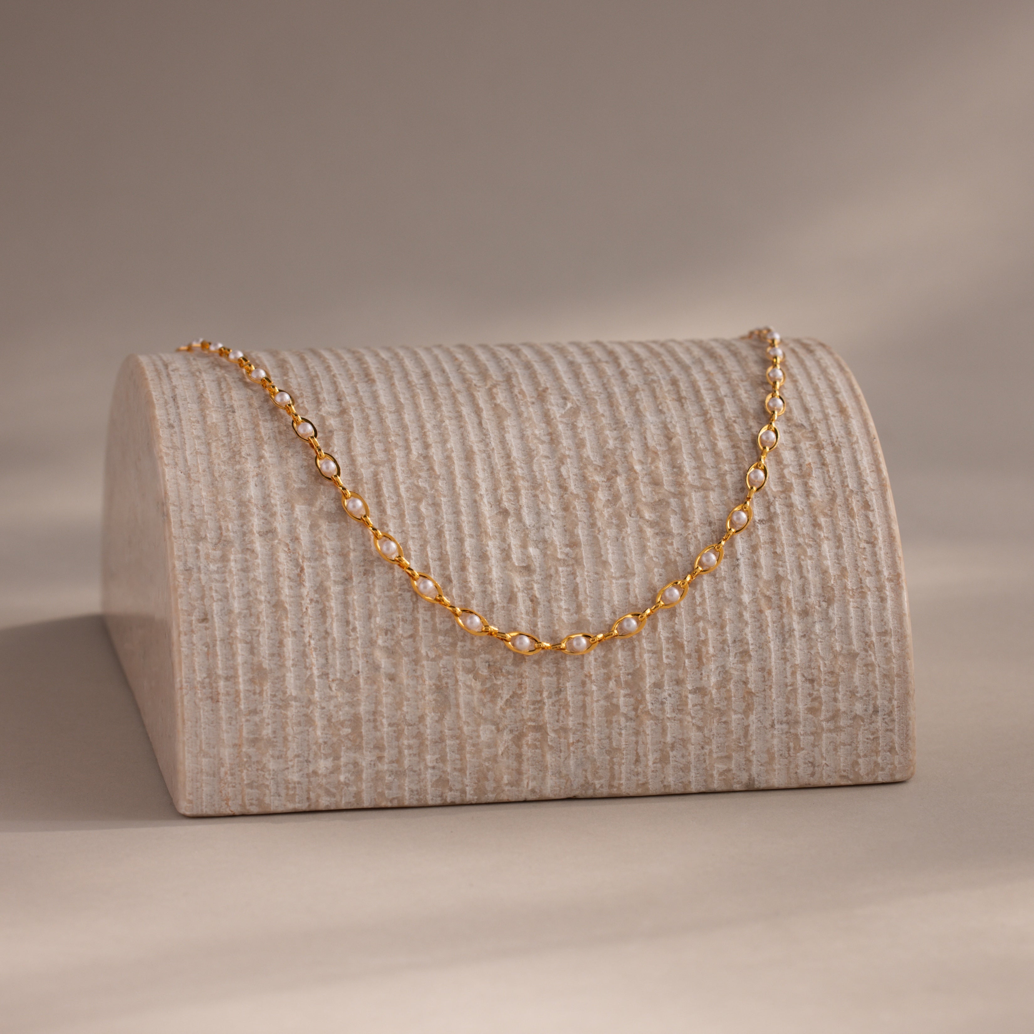 Pearl chain necklace draped over a textured display stand, softly lit in a warm, minimal setting.