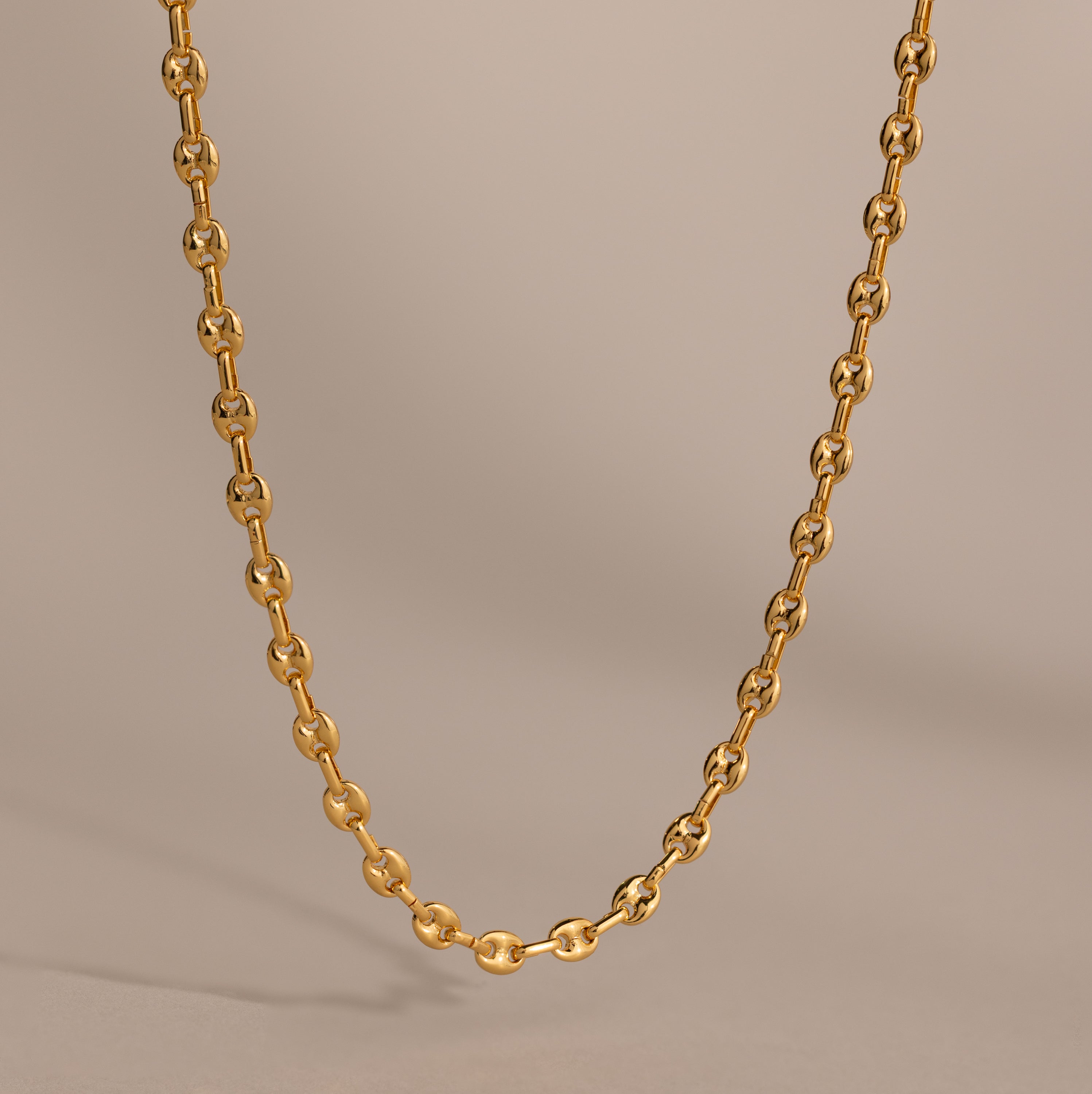 Gold mariner chain necklace with polished oval links, displayed against a neutral beige background.