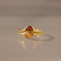 The Sculpted Toi et Moi Ring Set in 18K Gold features two gold rings with pear-shaped red and yellow gemstones, elegantly stacked on a smooth reflective surface.