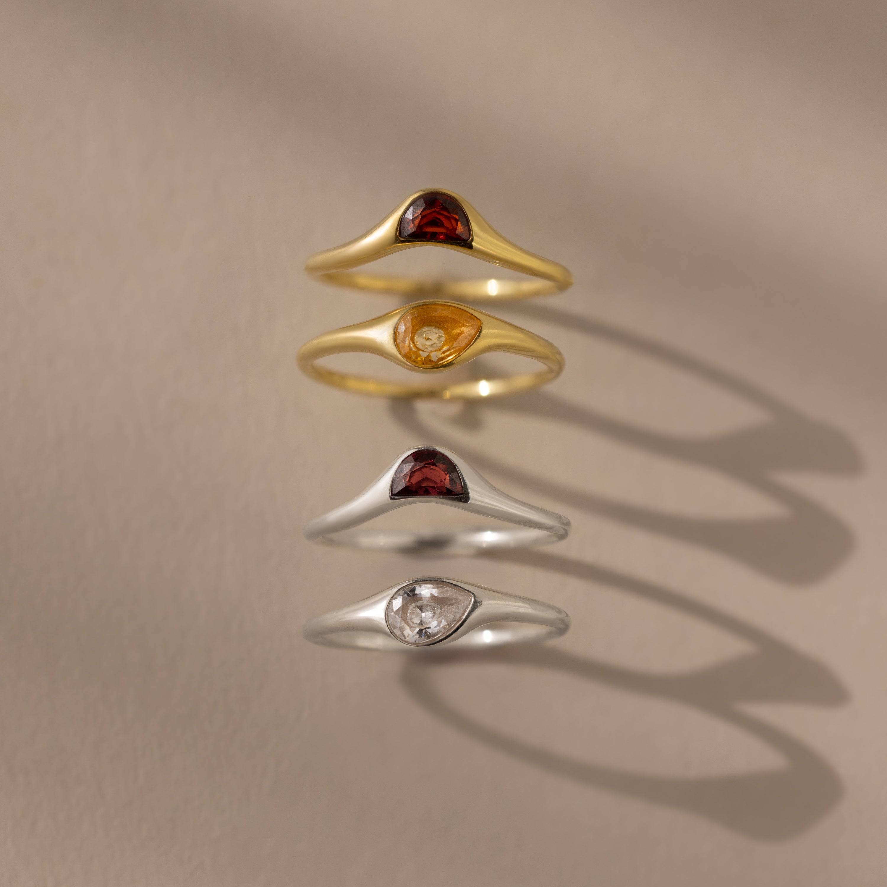 The Sculpted Toi et Moi Ring Set features four gold and silver rings with teardrop-shaped stones, ideal for stacking or making a statement. Their delicate design casts soft shadows on beige, enhancing any look.