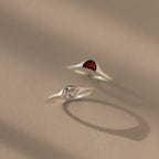 The Sculpted Toi et Moi Ring Set in Silver features two minimalist silver rings—one with a red gemstone, one with a clear stone—displayed on a neutral background.