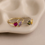 The Love Toi et Moi Ring features heart-shaped gemstones on gold and silver bands, perfect for stacking and displayed on a stylish beige ceramic dish.